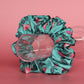 A teal scrunchie with a floral pattern of pink and dark green leaves. 
