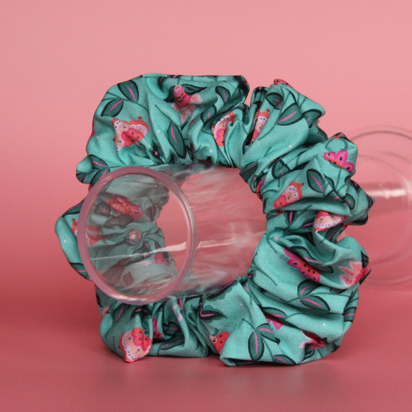 A teal scrunchie with a floral pattern of pink and dark green leaves. 