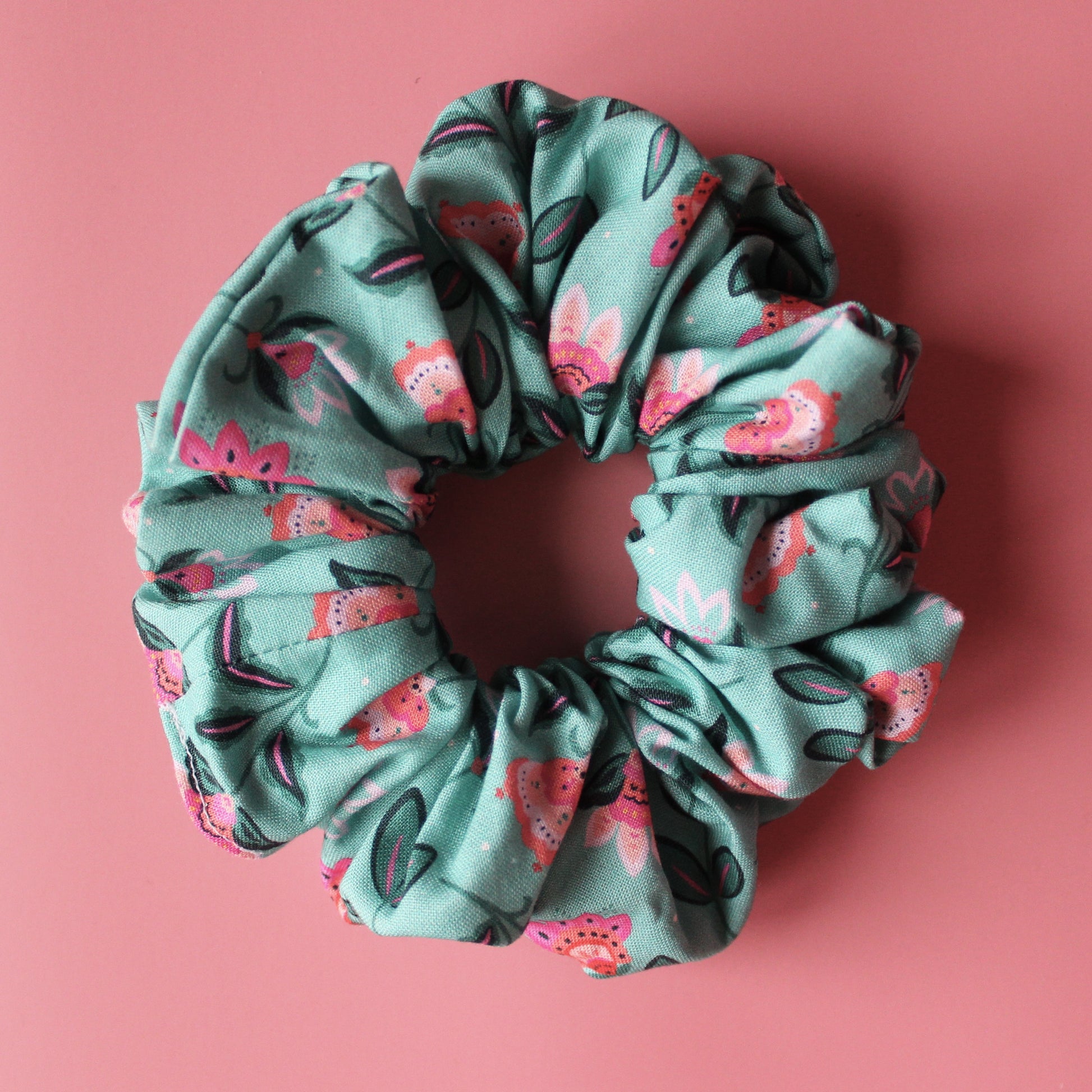 A teal scrunchie with a floral pattern of pink and dark green leaves. 