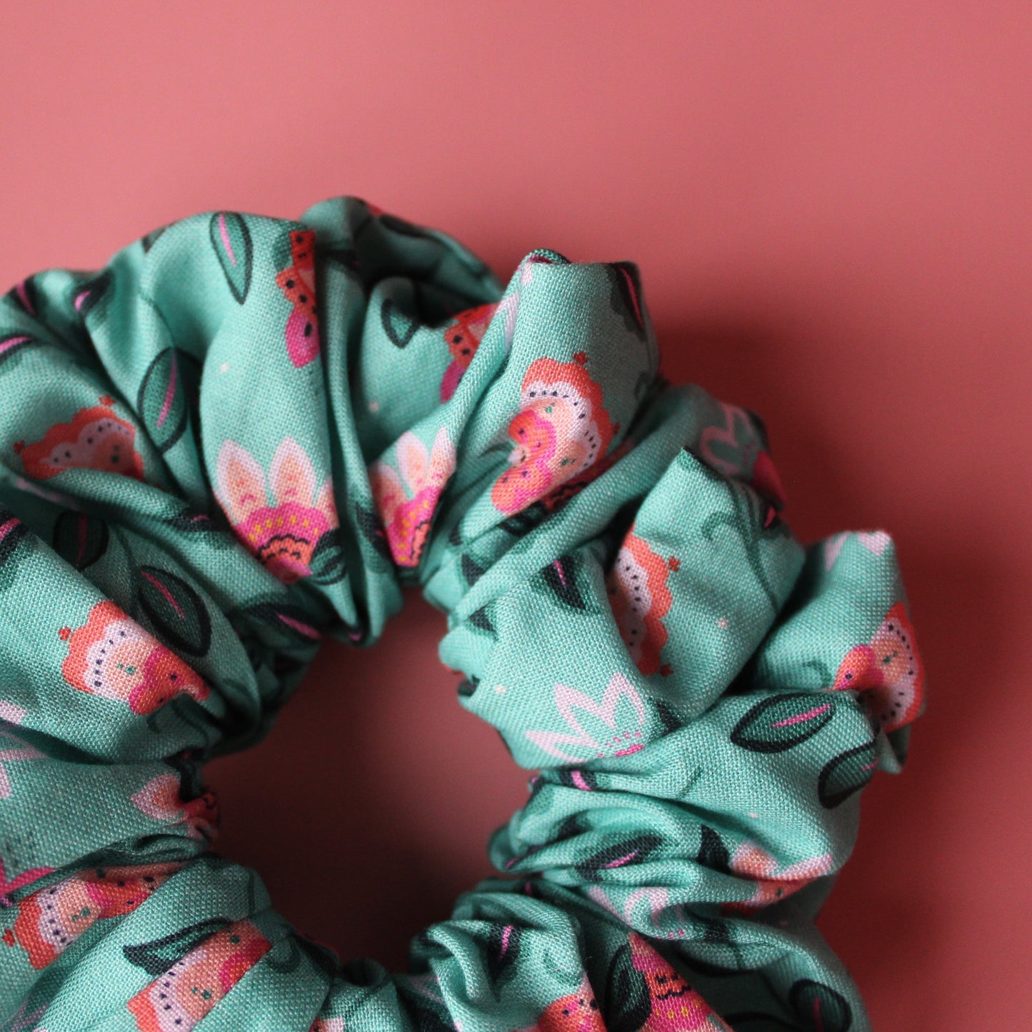A teal scrunchie with a floral pattern of pink and dark green leaves. 