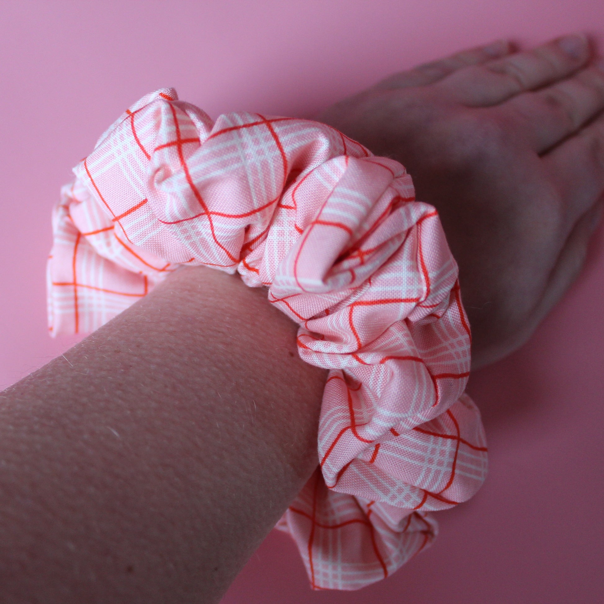 Pink oversized hair scrunchie with red and white check pattern on wrist