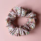 Floral patterned hair scrunchie in pink with white, yellow and green all over pattern. 