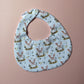 Baby bib with cute pig pattern. White background with pink pigs on bed of barley.