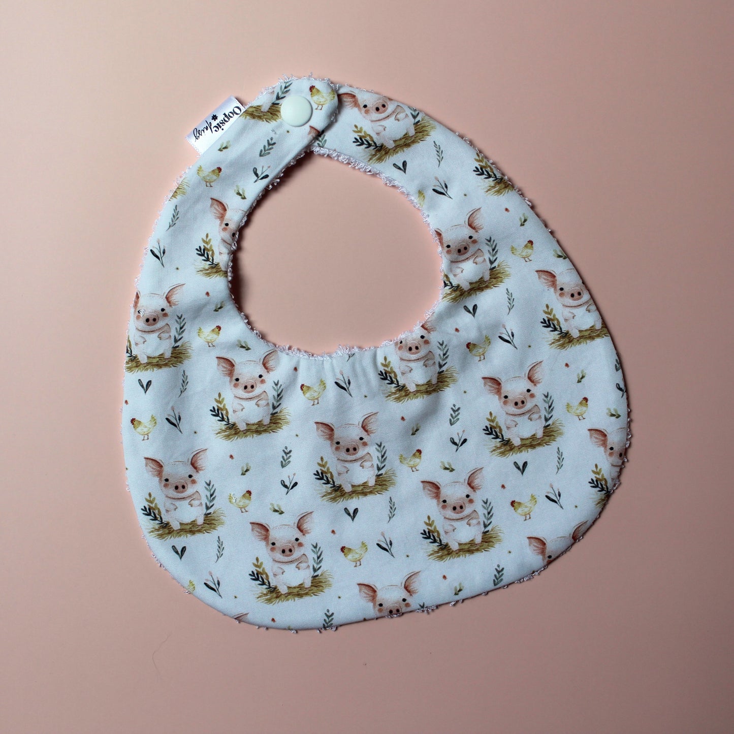Baby bib with cute pig pattern. White background with pink pigs on bed of barley.