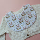 Baby bib with cute pig pattern. White background with pink pigs on bed of barley.