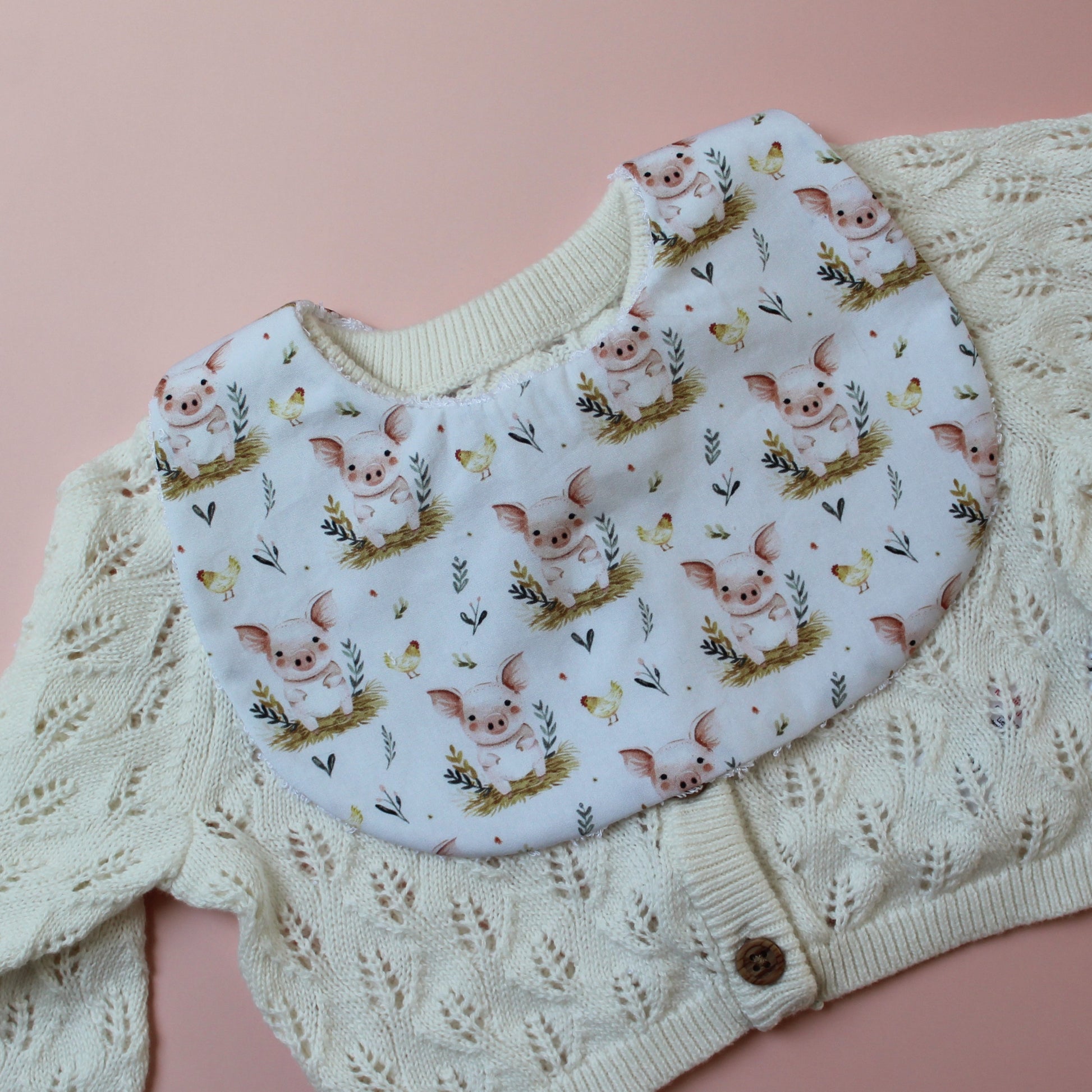 Baby bib with cute pig pattern. White background with pink pigs on bed of barley.