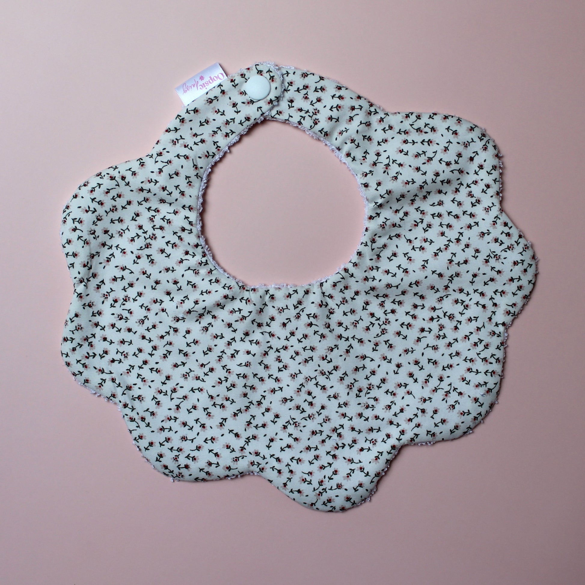 Scallop baby bib with small ditsy floral pattern. Cream background with pink flowers