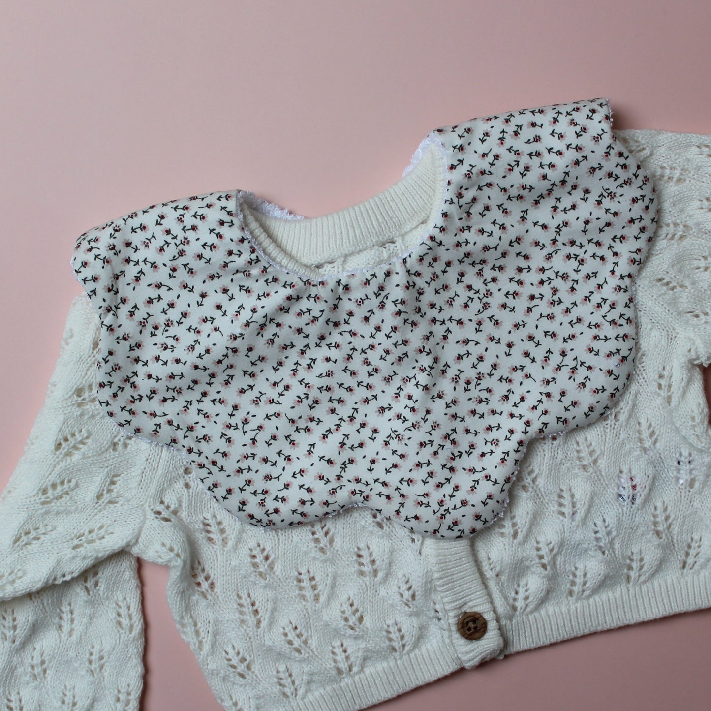 Scallop baby bib with small ditsy floral pattern. Cream background with pink flowers