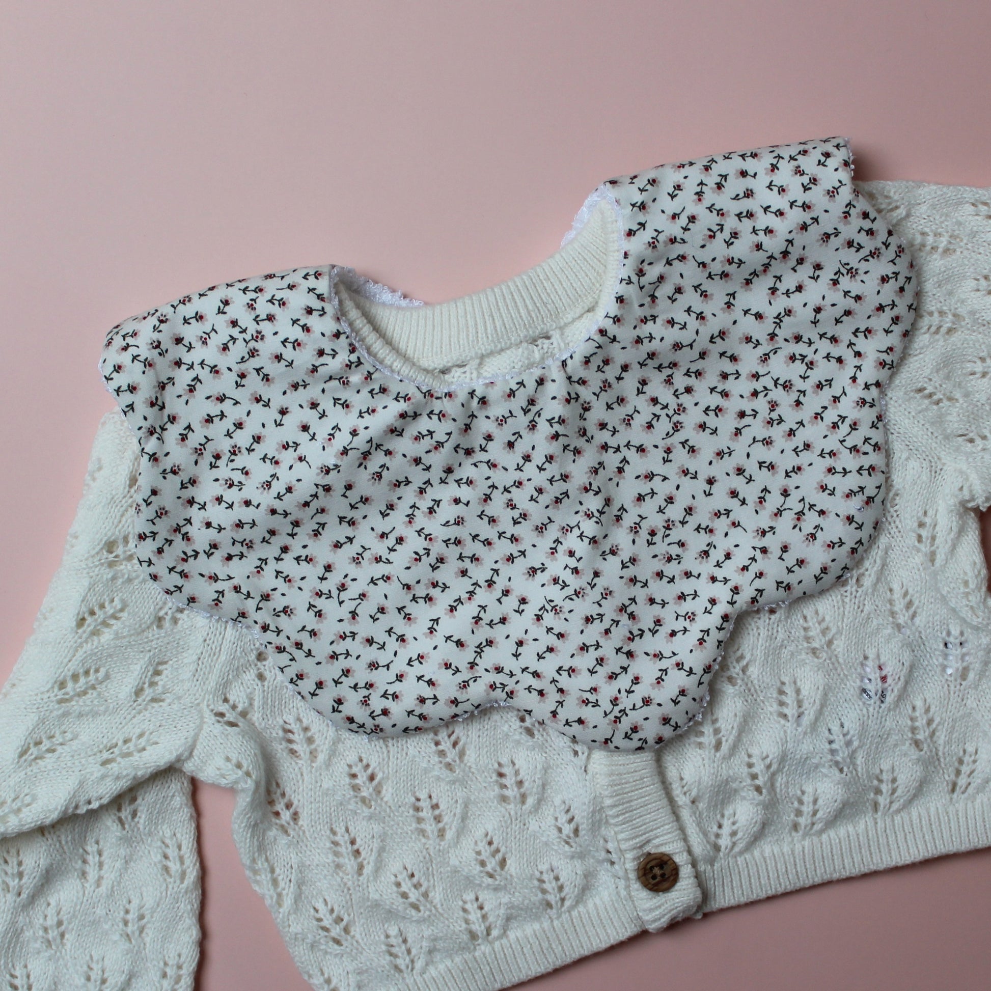 Scallop baby bib with small ditsy floral pattern. Cream background with pink flowers