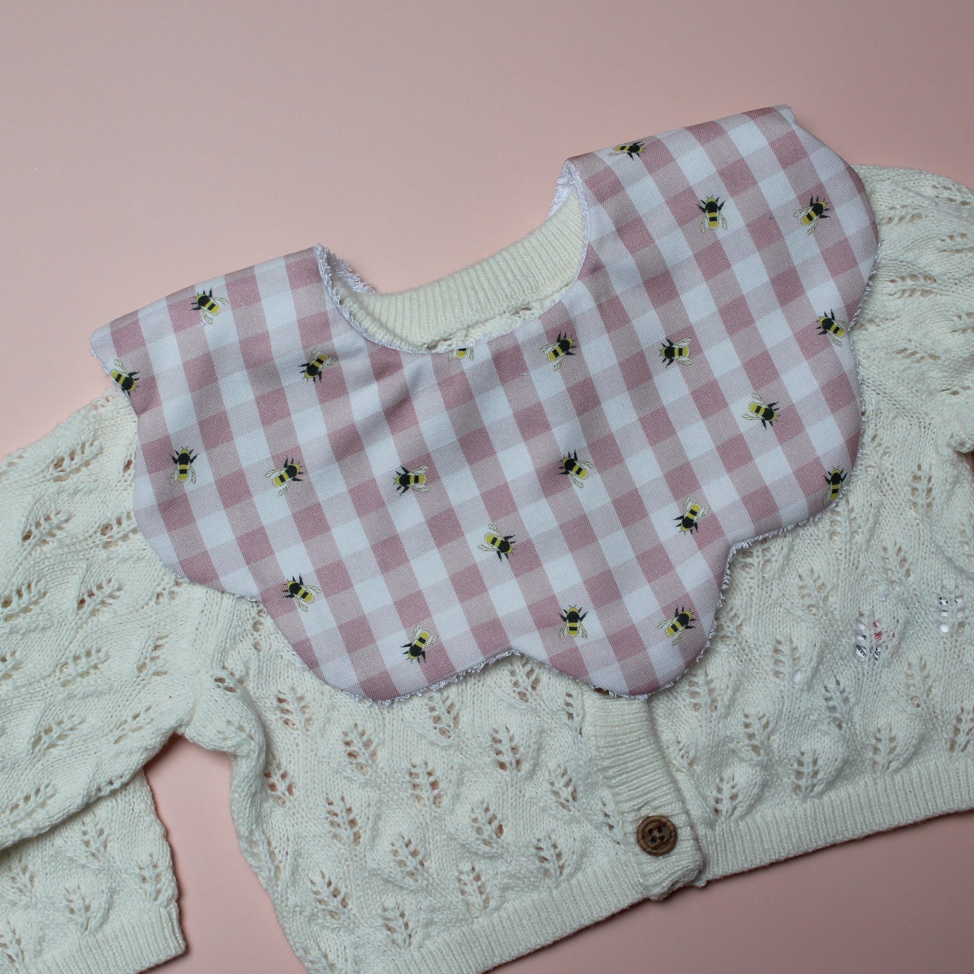 Gingham scallop baby bib in pink and white with little bee pattern.