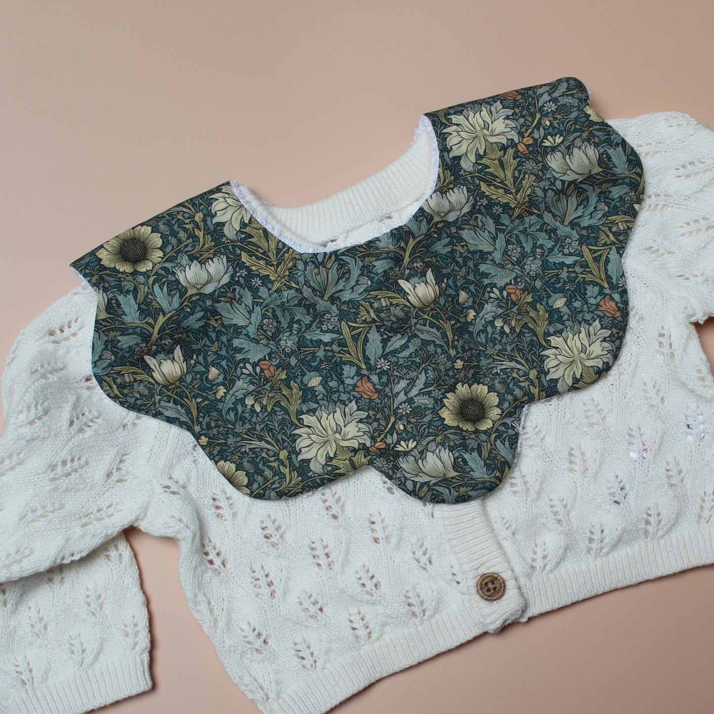 Scallop baby bib in dark green with yellow/ orange all-over floral pattern