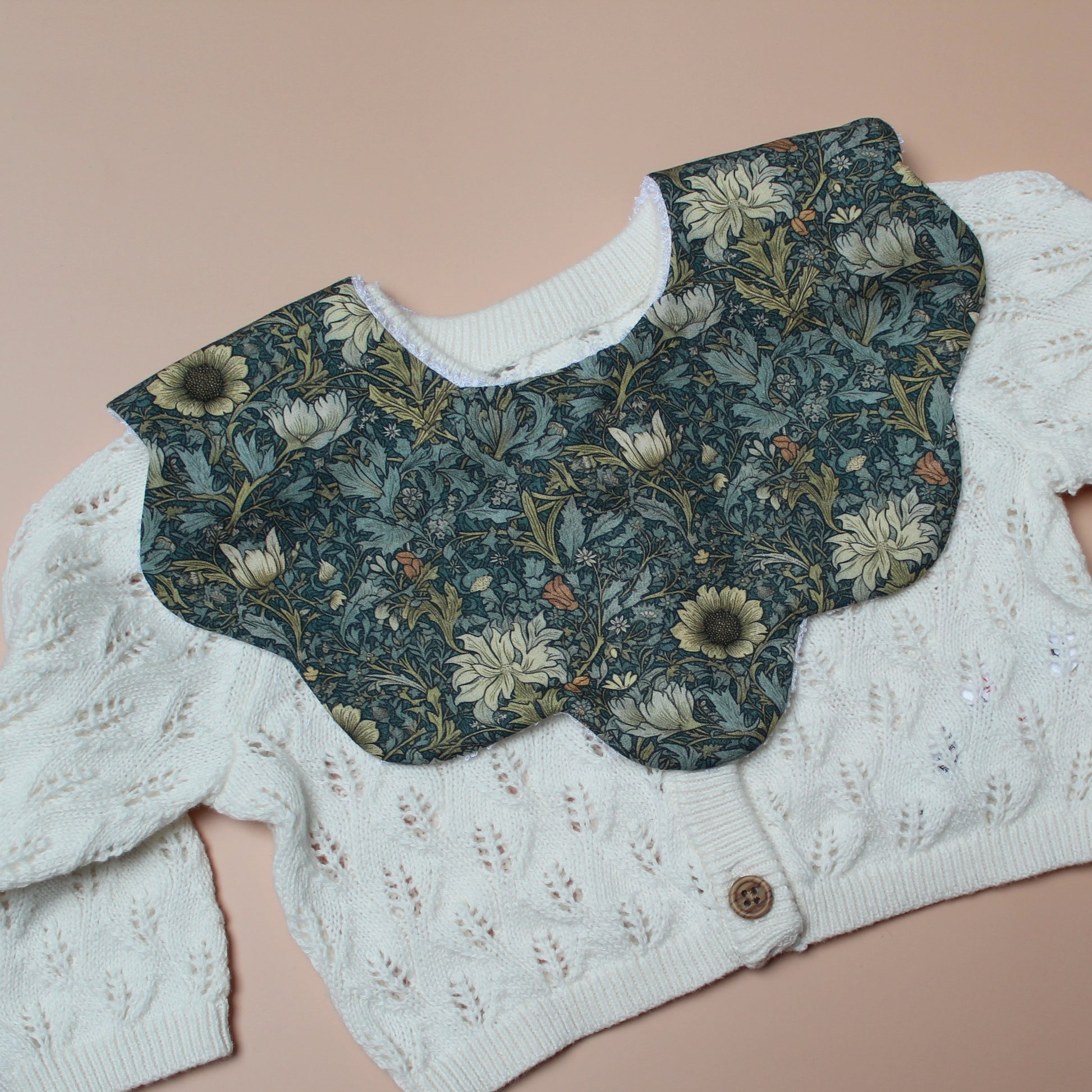 Scallop baby bib in dark green with yellow/ orange all-over floral pattern