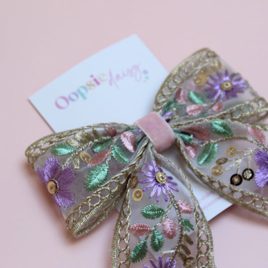 Embroidered hair bow with pink and purple flowers and gold sequins. 