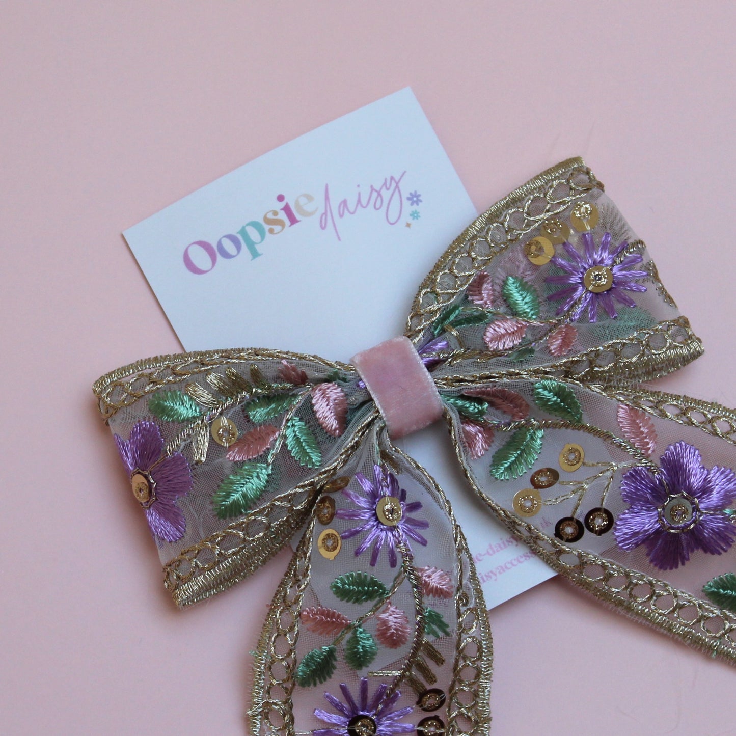 Embroidered hair bow with pink and purple flowers and gold sequins. 