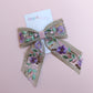 Embroidered hair bow with pink and purple flowers and gold sequins. 