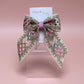 Hair bow with pink, green and gold shimmer embroidered crisscross pattern