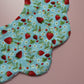 A close-up of a fabric baby bib featuring a blue background with a strawberry and white flower print, laid on a pink background.