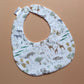 A fabric baby bib with a safari animal print, featuring zebra, giraffe, elephant and lion illustrations on a white background.