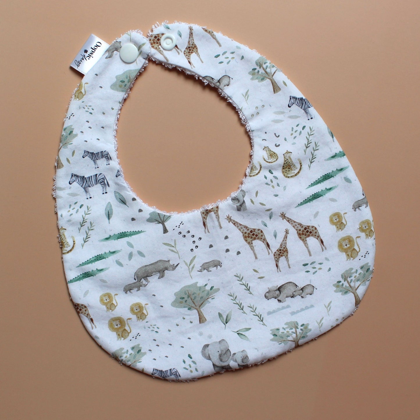 A fabric baby bib with a safari animal print, featuring zebra, giraffe, elephant and lion illustrations on a white background.