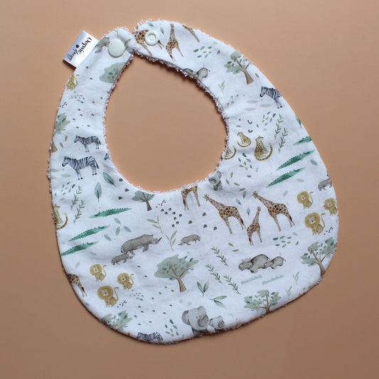 A fabric baby bib with a safari animal print, featuring zebra, giraffe, elephant and lion illustrations on a white background.