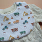 A close-up of a baby bib with a white background and a colourful construction vehicle print, laid over a cream-coloured cable-knit cardigan.