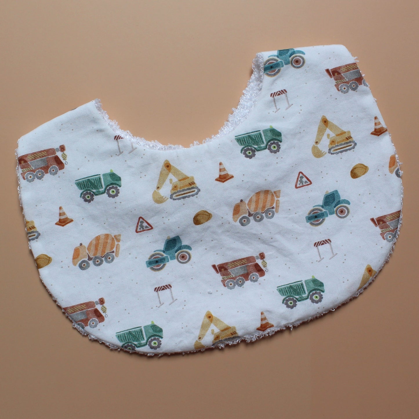A close-up of a baby bib with a white background and a colourful construction vehicle print with diggers, lorries and cranes.