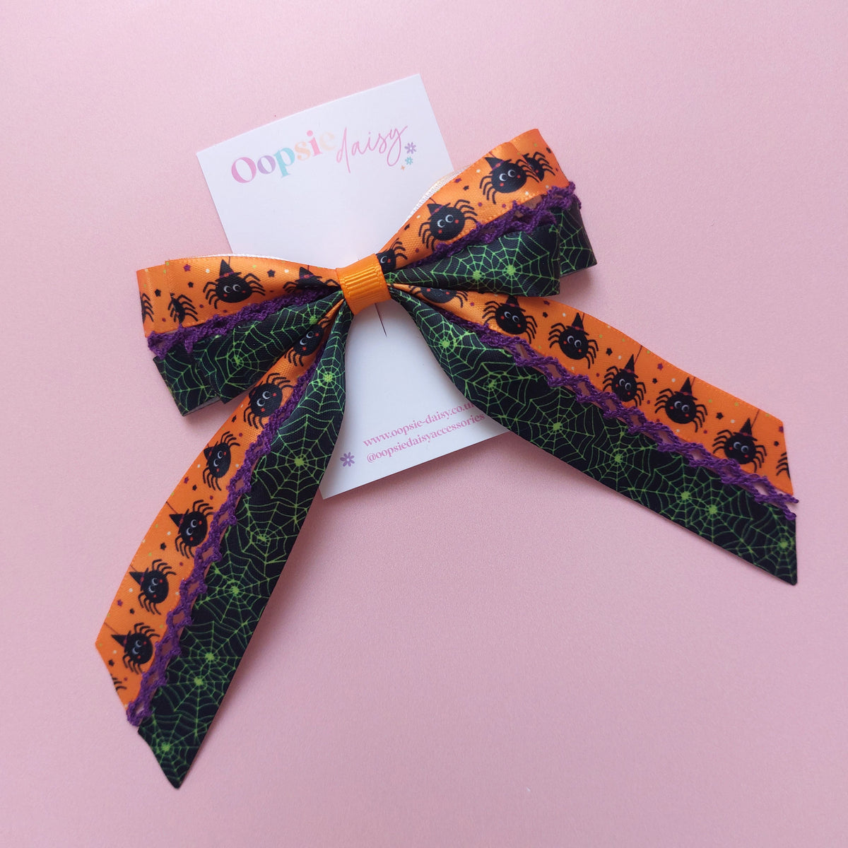 A Halloween-themed fabric hair bow with orange, black, and purple spider and spiderweb patterns.